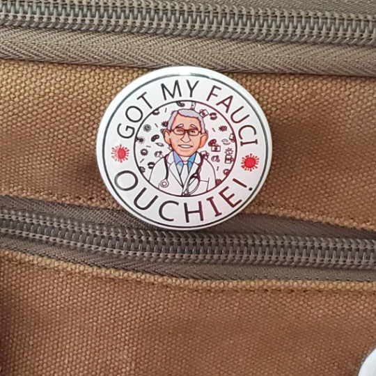 A pin with a cartoon of Anthony Fauci read “Got my Fauci ouchie!”