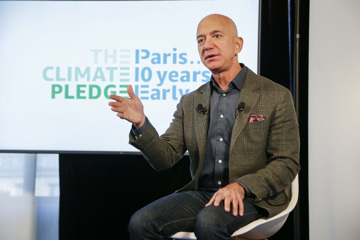 Jeff Bezos onstage speaking in front of a screen that reads “The climate pledge. Paris ... 10 years early.”
