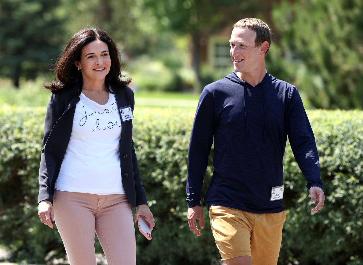 Sheryl Sandberg and Mark Zuckerberg walking past shrubbery on a sunny day.