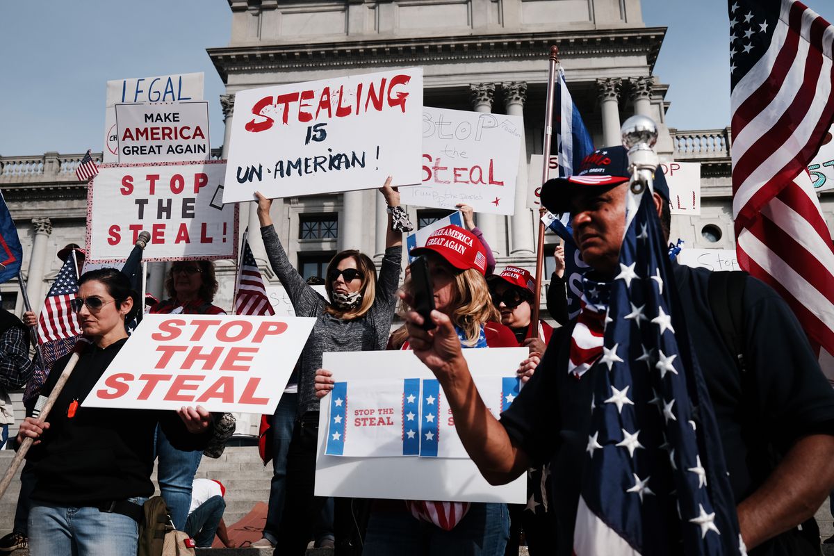 Protesters hold signs that read “Stop the steal,” “Make America great again,” and “Stealing in un-American!”