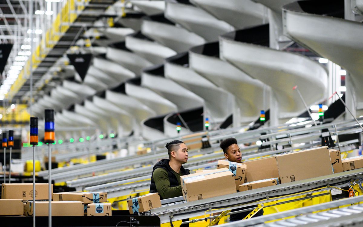 Workers at an Amazon fulfillment center look at boxes going up one of many conveyor belts.