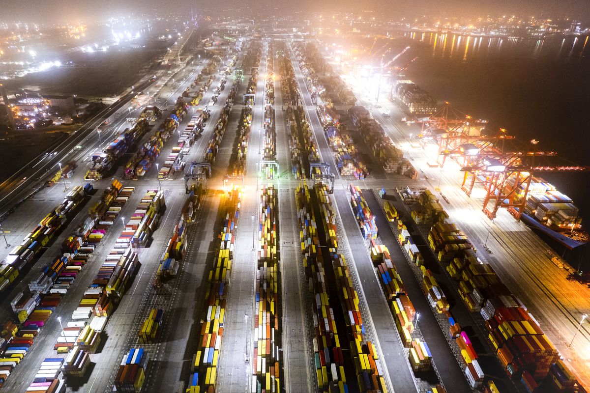 An aerial view of containers on land at a port at night with bright lights shining.