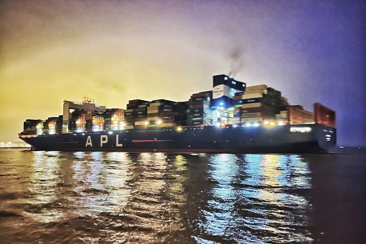 A loaded container ship on the water at night with lights shining.