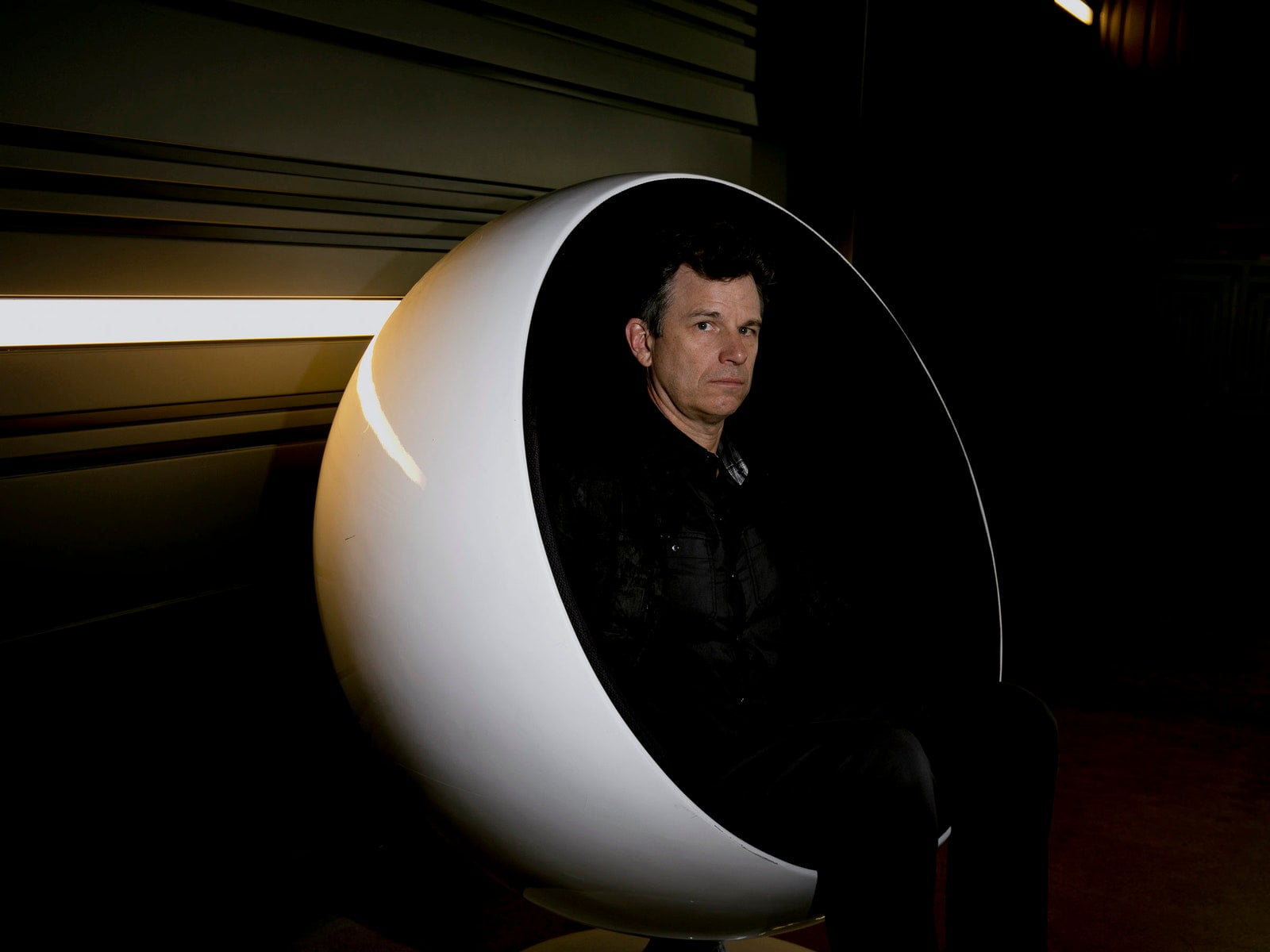 Person sitting in white egg chair against a black wall with light beams